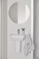Waschbecken von Ideal Standard, montiert an der Wand, mit einem grauen Handtuch daneben, und einem kleinen Behälter mit Utensilien auf der Ablage. Spiegel darüber.